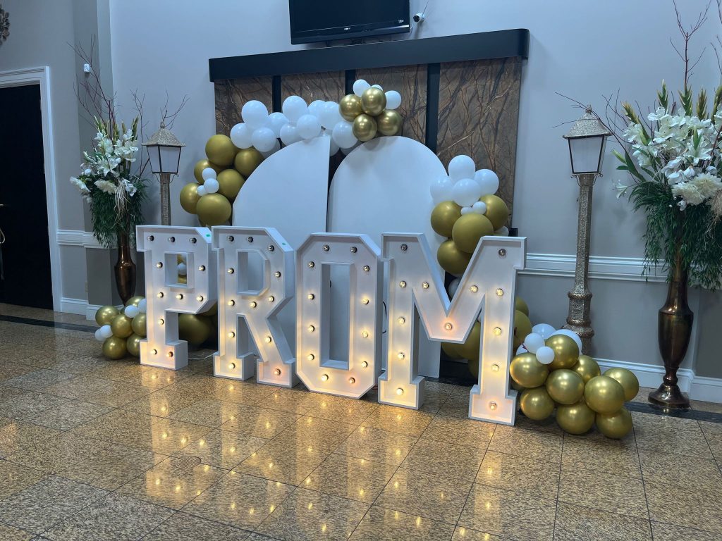 Marquee letters in Oakville that spell out "PROM" with a chiara arch and balloons framing the display.