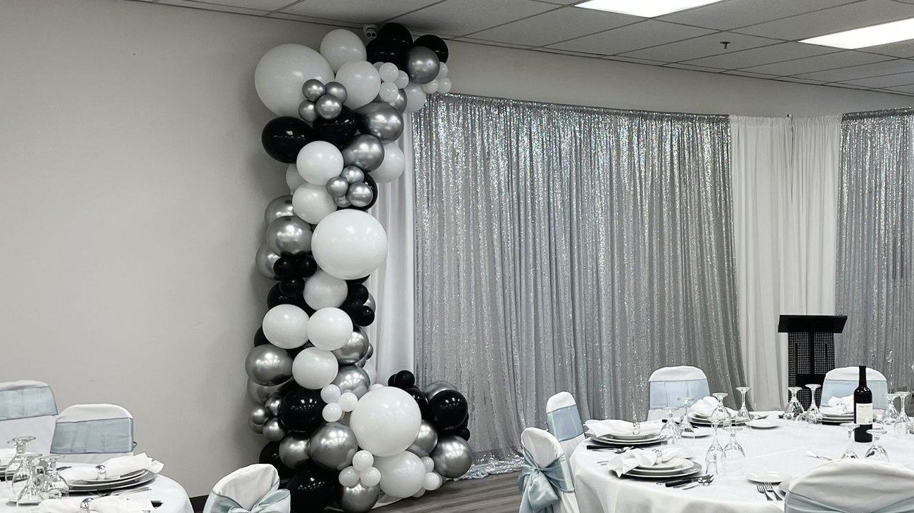A single balloon column in white, black and silver against a pale wall in a set room