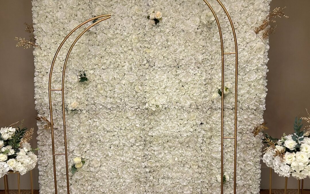 A white floral wall with a gold arch frame and matching floral urns either side