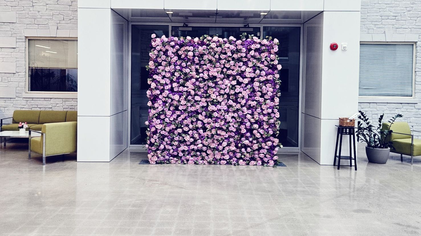 A lavender and purple rose flower wall standing in a bright atrium with white panelling and pale brick