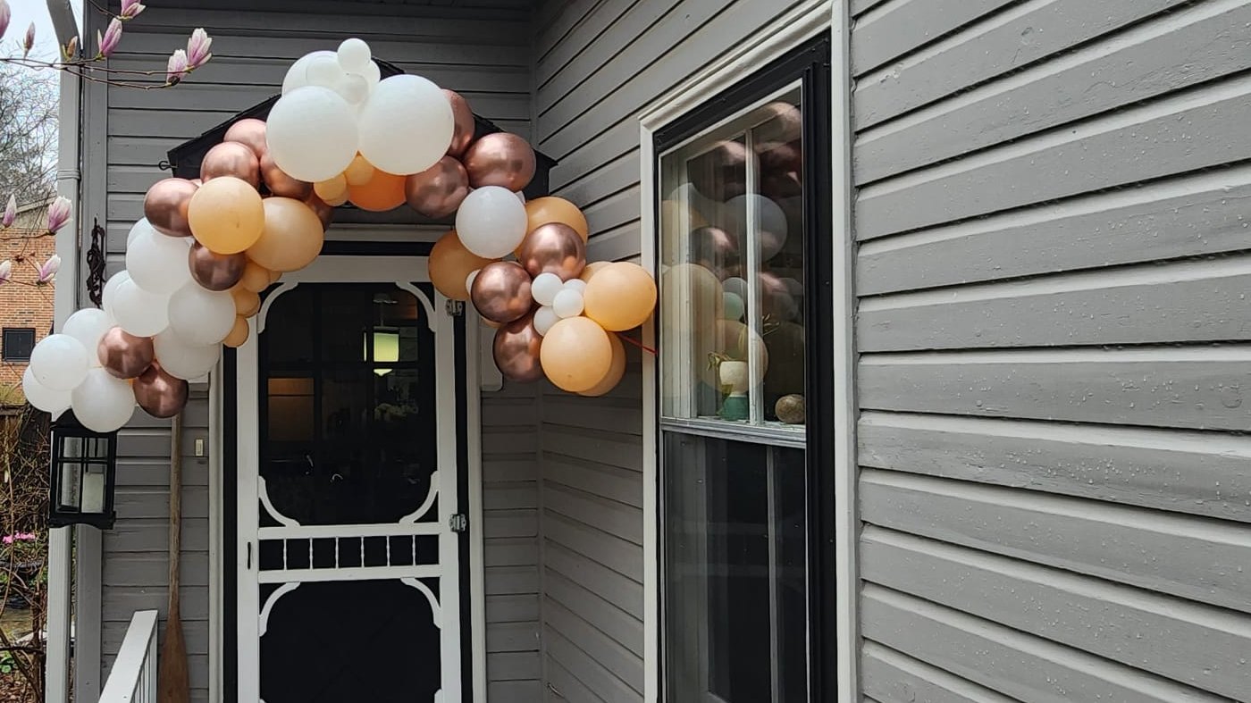 A rose gold, peach and white balloon arch framing a front door entrance