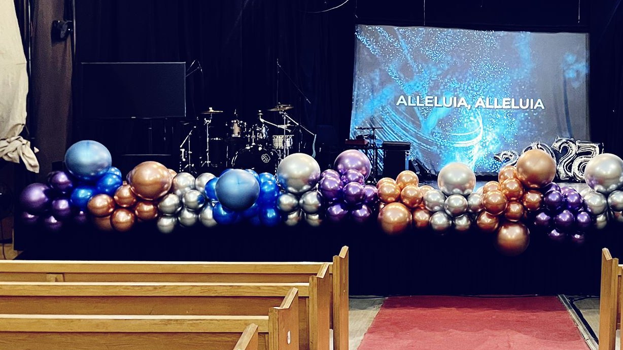 A chrome balloon garland in blue, purple, silver and rose gold running the length of a stage front