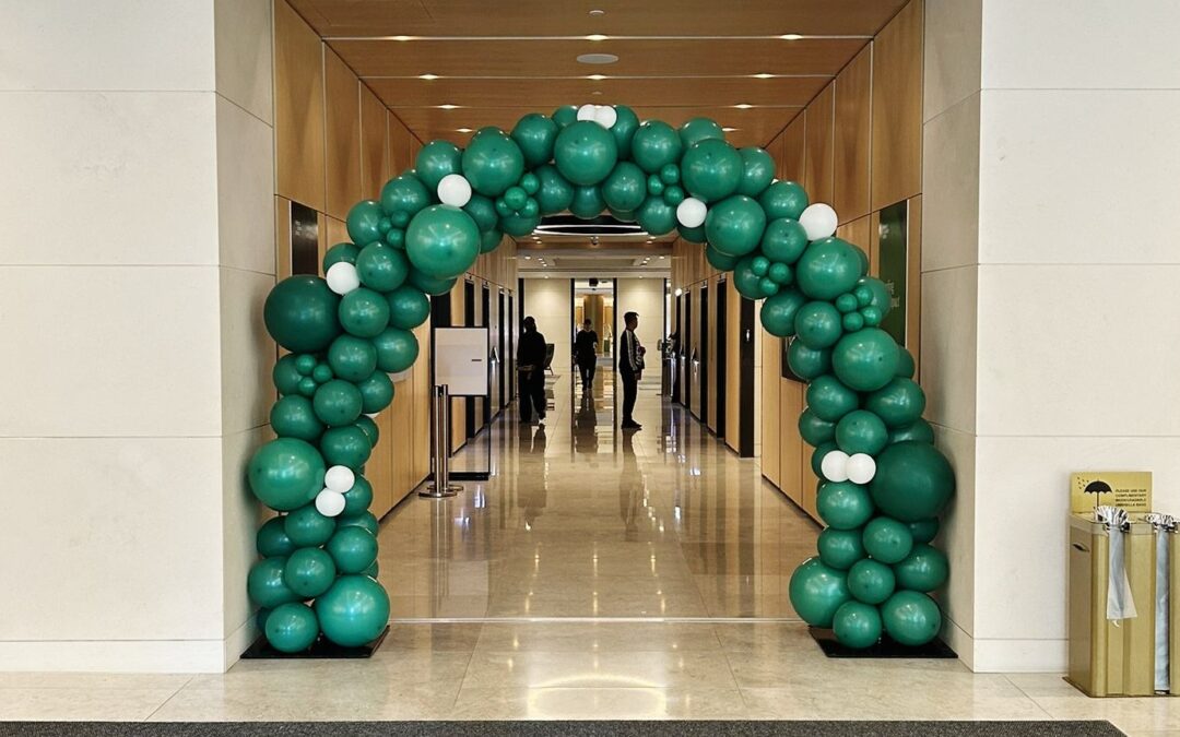 A green and white balloon arch framing a corridor entrance in an office lobby