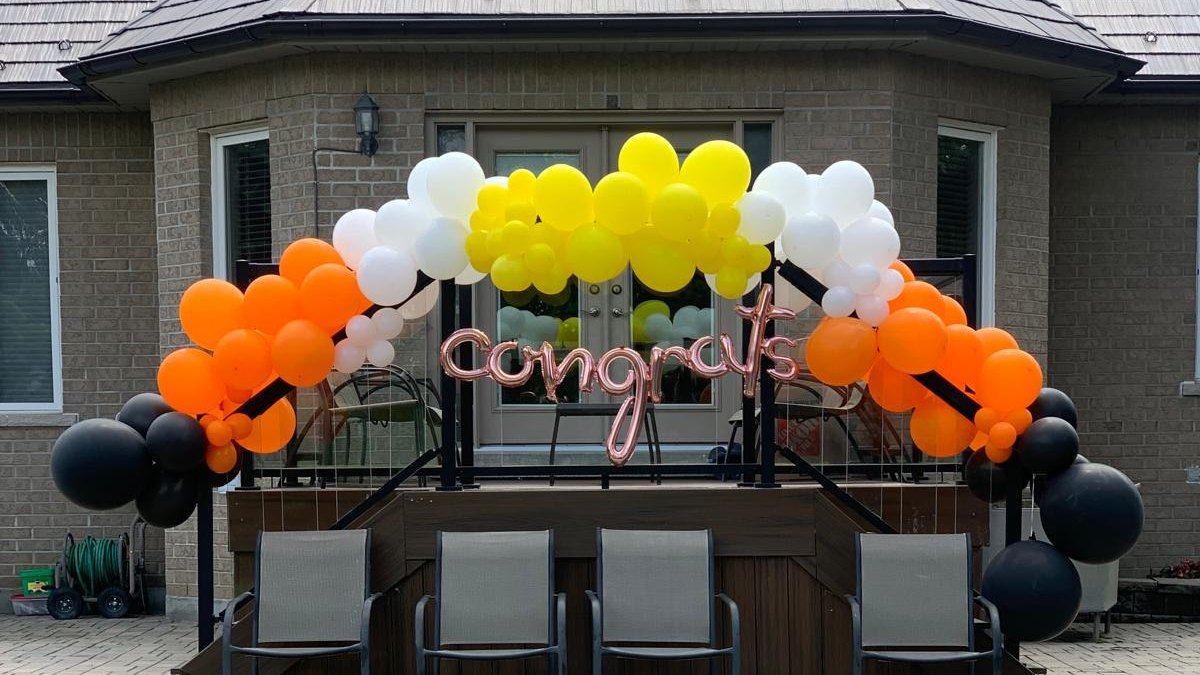 An orange, yellow, white and black balloon arch over a patio bar against a pale brick wall